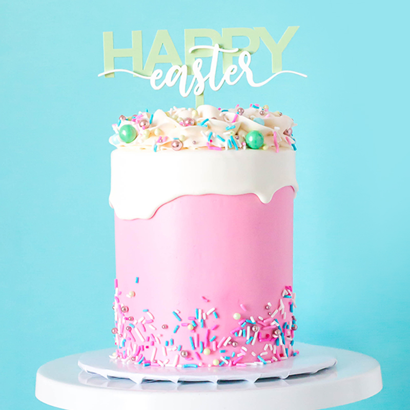 Pink cake with white frosting and colorful sprinkles with a "Happy Easter" cake topper by Zoi&Co