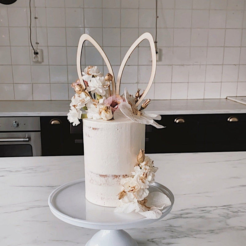Cake by @rosiesthecakestudio on kitchen top with floral decorations and zoiandco minimal bunny ear cake topper